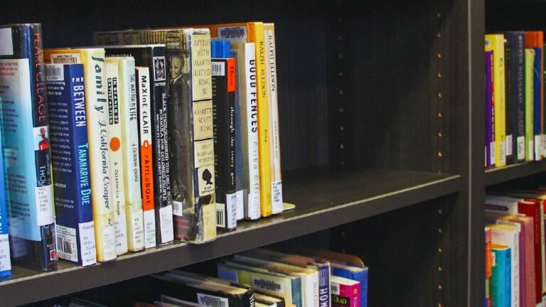 A group of Raleigh marching band members in uniform, holding saxophones, smile and pose for the camera on an outdoor track with trees in the background.